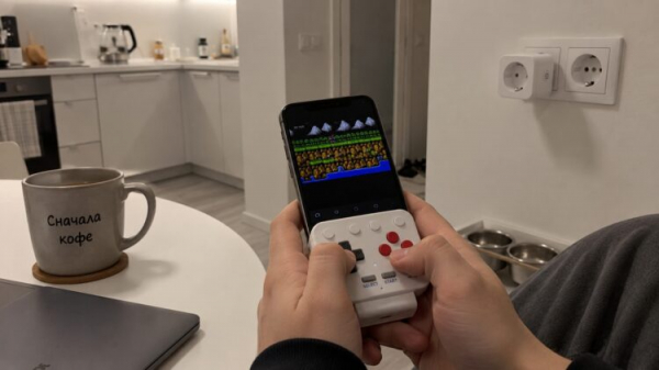 Смартфон, вдетый в геймпад 8BitDo FlipPad, в руках. Фото.