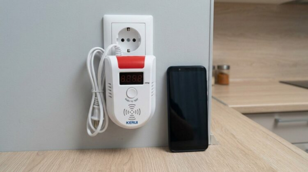 Датчик газа KERUI GD13 на розетке рядом со смартфоном